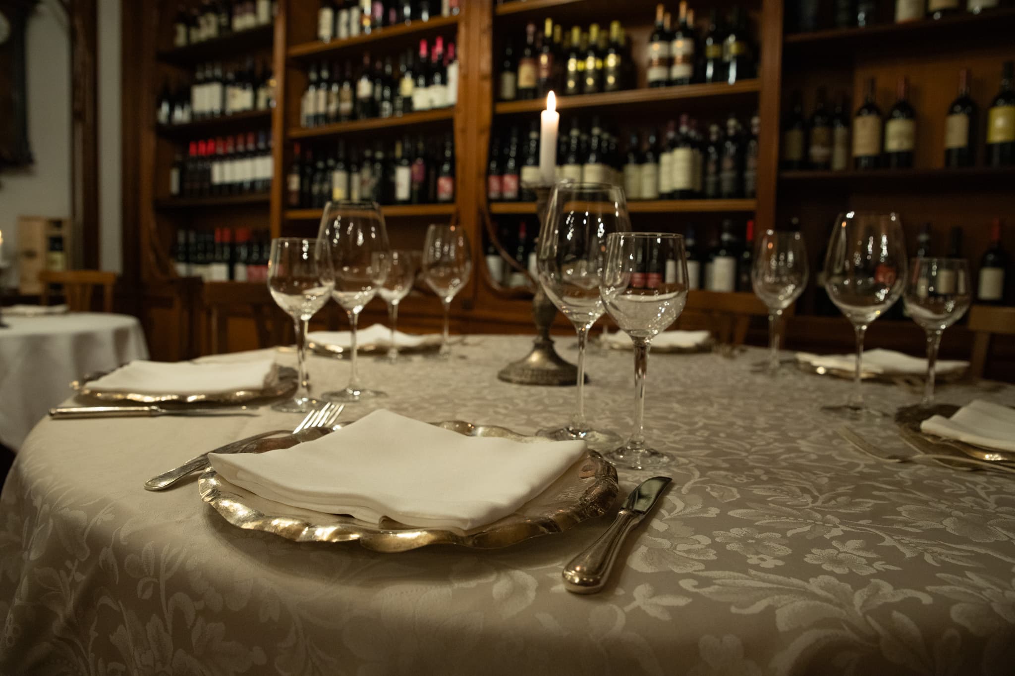 Tavolo apparecchiato con calici e argenteria davanti alla parete dei vini